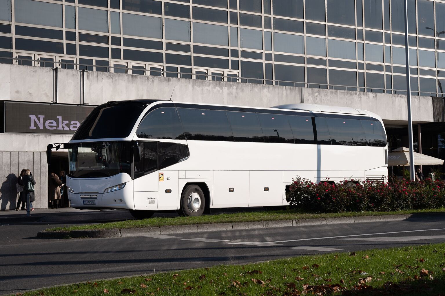 Bijeli autobus Neoplan Cityliner parkiran ispred staklene zgrade, snimljen sprijeda iz tri četvrtine