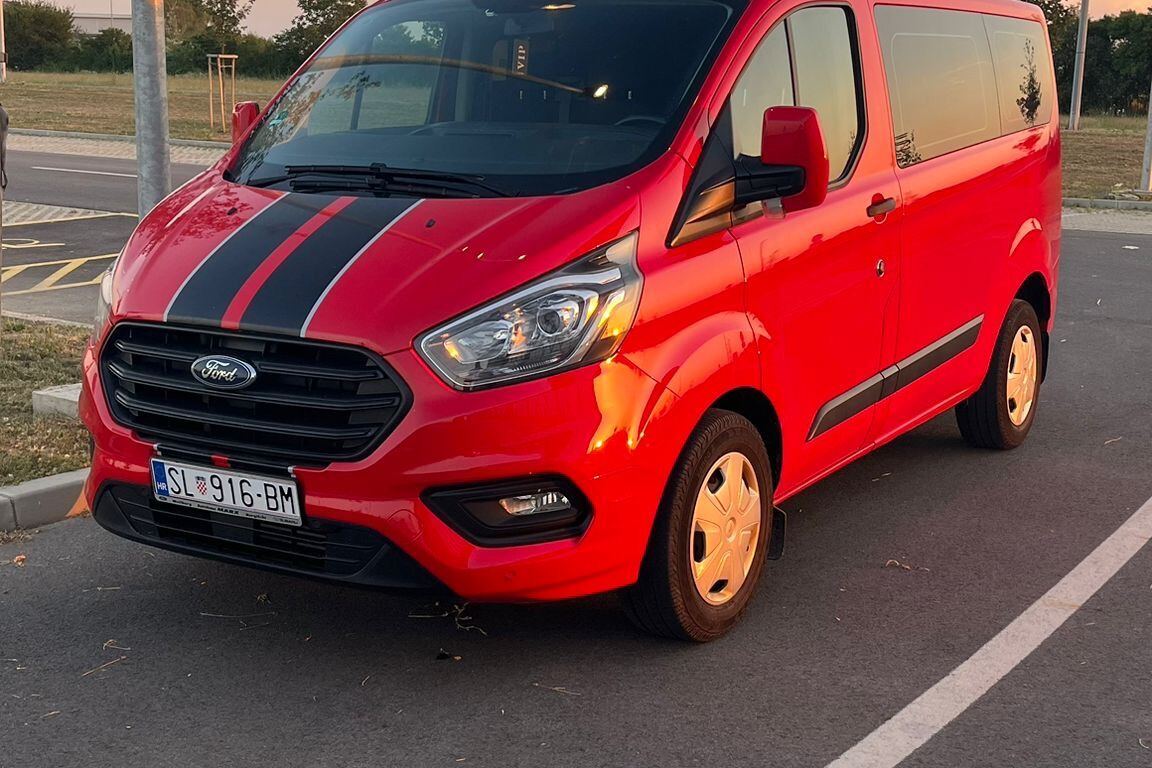 Crveni kombi Ford s crnim prugama, snimljen sprijeda iz tri četvrtine na parkiralištu
